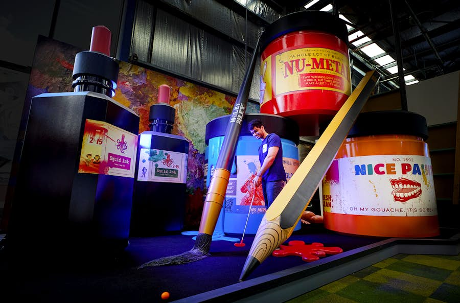 Man playing golf around giant paint jars