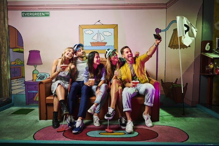 A group of five friends sitting on the couch at the '742 Evergreen Terrace' hole taking a selfie.
