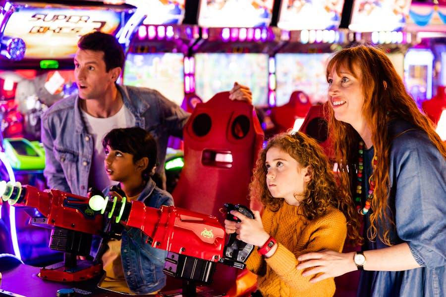 Two adults watch on and help two kids playing an arcade game at Archie Brothers.