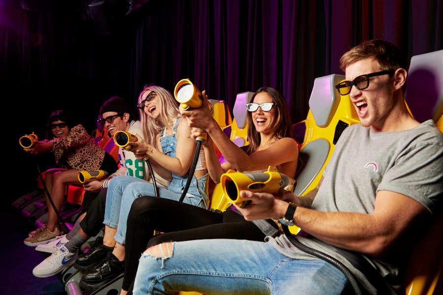A group of 5 friends in the XD theatre at Archie Brothers, with 3D glasses on and using the laser gun to hit targets on the screen.