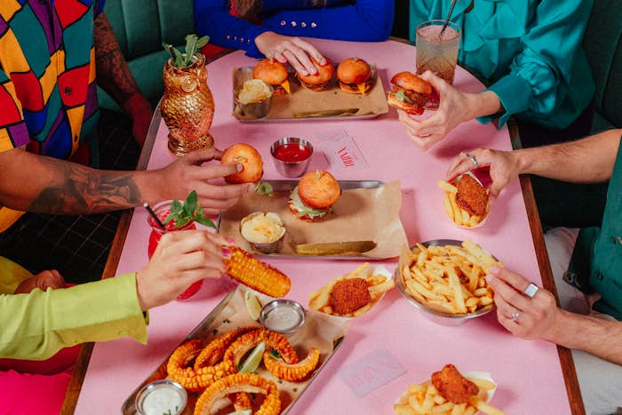 A group of people sitting around an assorted selection of sliders, fries, chicken wings and corn ribs.