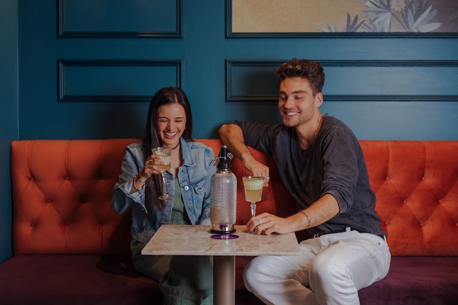 Two people smiling and laughing while sitting on a lounge at La Di Darts. They are drinking a signature La Di Darts cocktail.