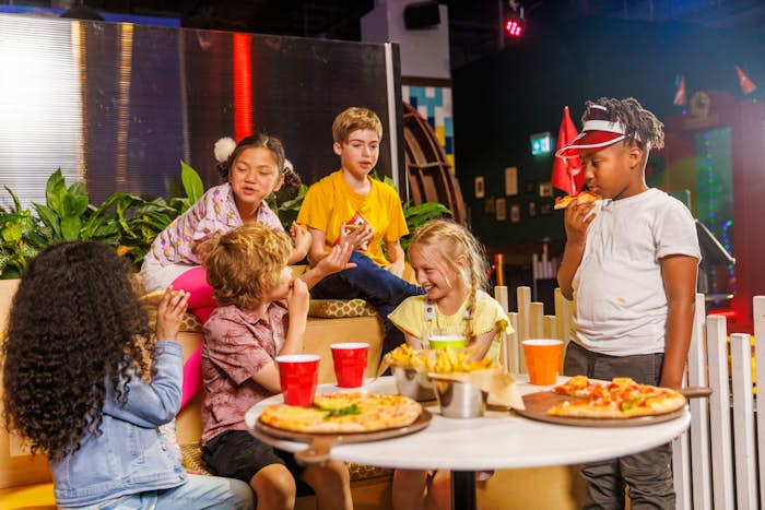 Group of children sitting around a table with pizza and drinks
