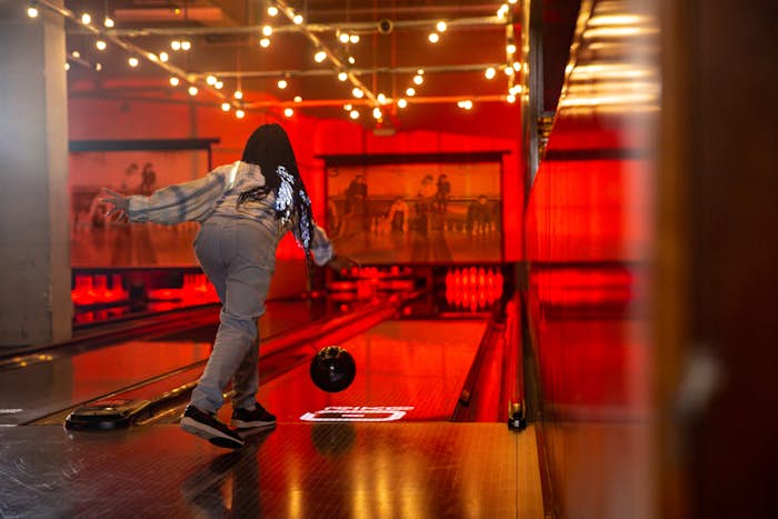 Teenage girl releasing bowling ball down lane