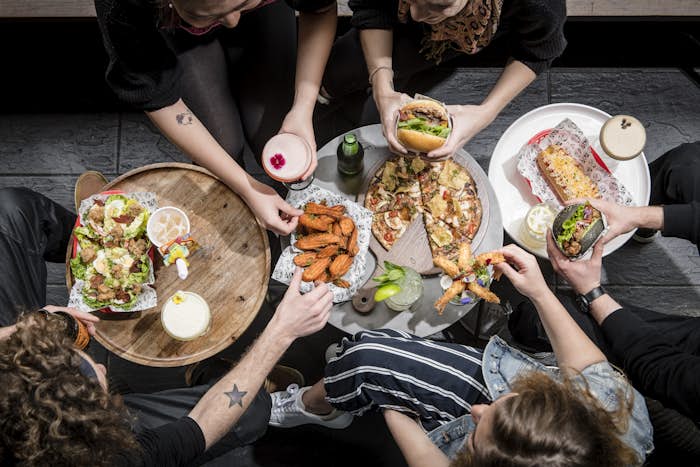 Group of people eating pizza, hot chips, hot dogs and salad with cocktails.