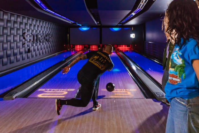 Man releasing bowling ball on the lanes with woman looking on in the background