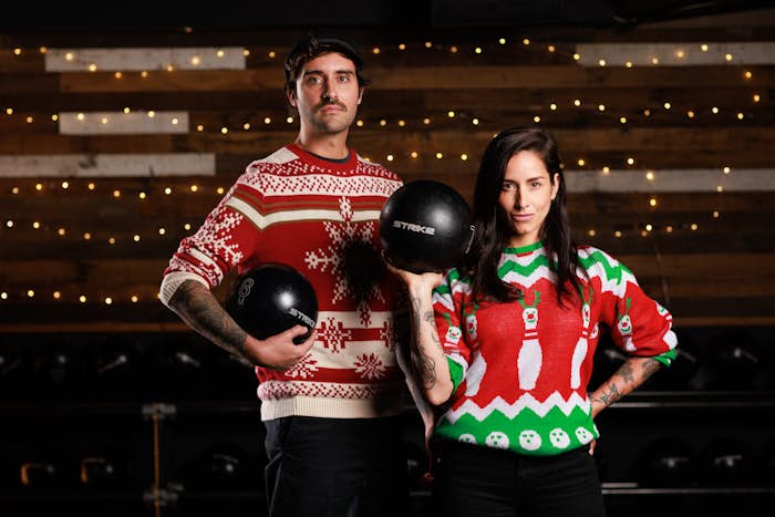 Man and woman holding strike bowling balls wearing Christmas Sweaters
