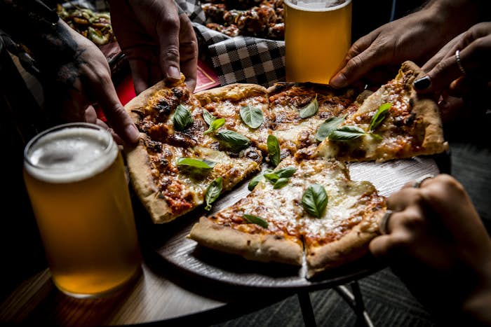 Hands pulling apart pizza with beers in foreground and background