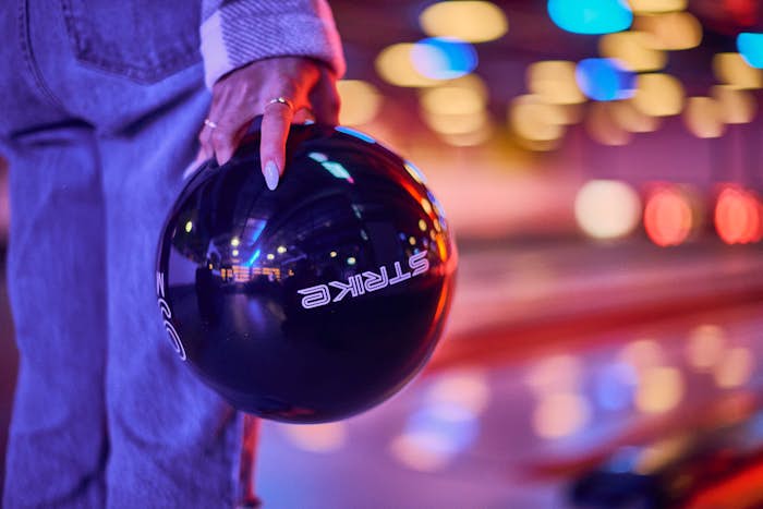 Woman holding Strike branded bowling ball in front of bowling lanes