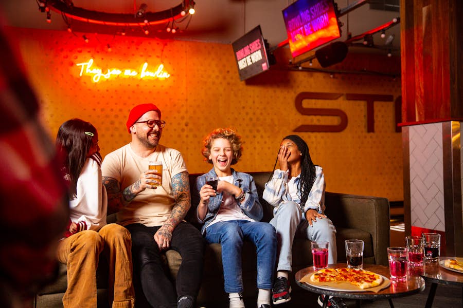 Family laughing on bowling lane with drinks and pizza