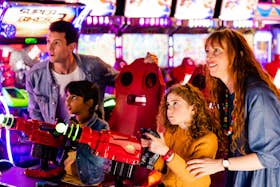 Mother, father and two kids playing arcade game with laser guns