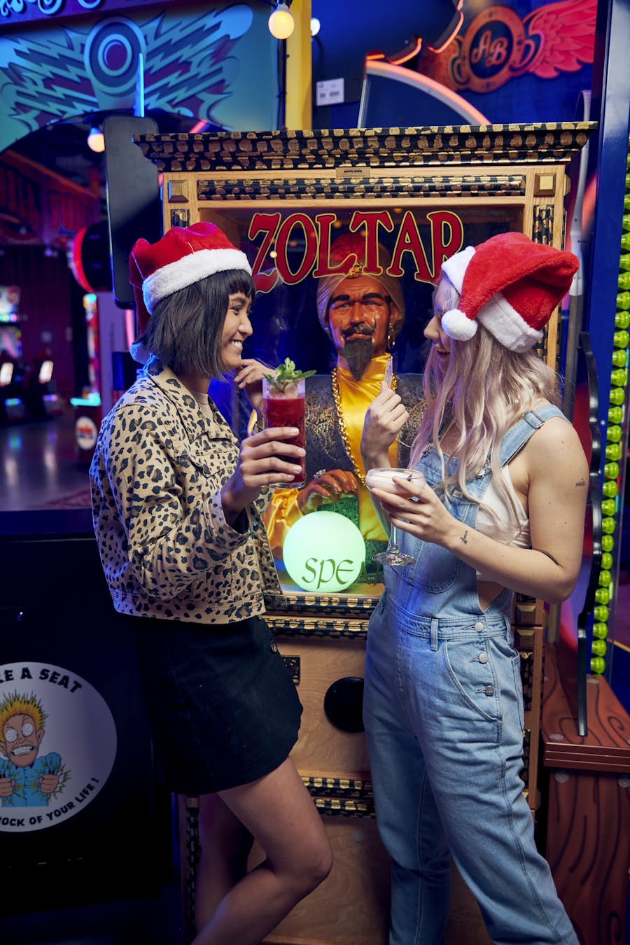 Two women standing by Zoltar arcade game wearing Santa hats