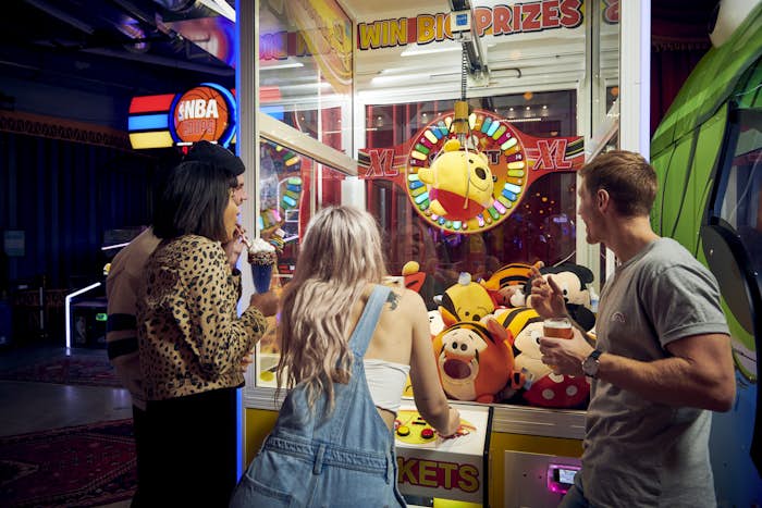 Group of friends watching a claw machine pick up a plush toy