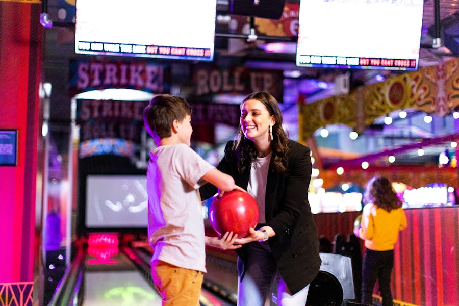 woman handing bowling ball to young boy