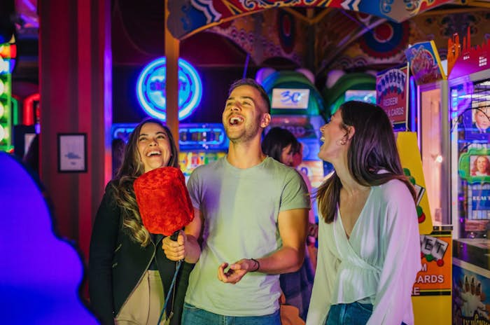 three friends laughing while playing on archie brothers arcade machines