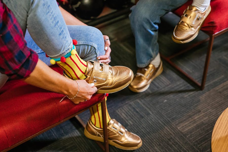 Woman fastening gold Strike branded bowling shoes whilst wearing yellow and red Strike socks