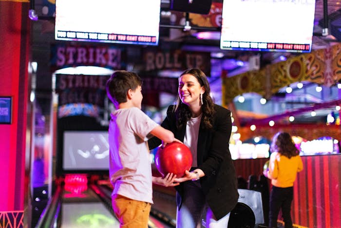 Woman handing child a bowling ball at Archie Brothers