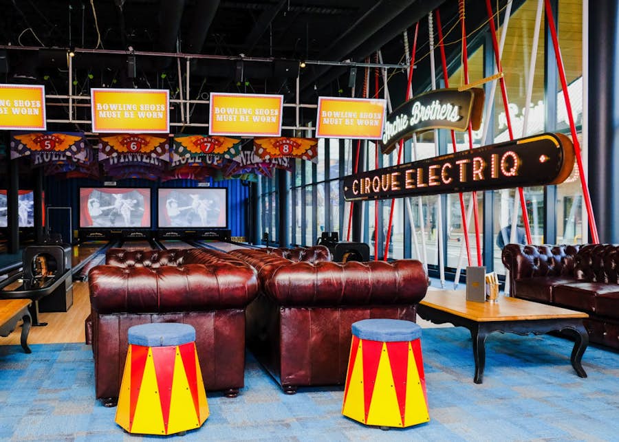 Bowling lanes and brown leather couches next to a large 'Archie Brothers Cirque Electriq' sign against the window at Archie Brothers Christchurch