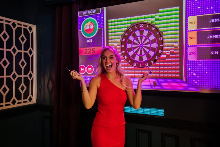 Girl in red dress celebrating in front of augmented darts board