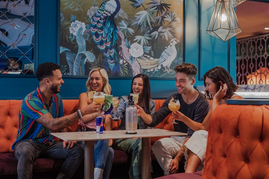 Group of 5 sitting in a booth toasting