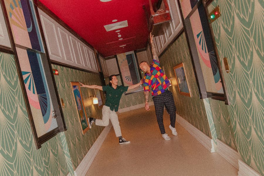 Two men pose in a hallway corridor styled as an illusions to look like everything is upside down.
