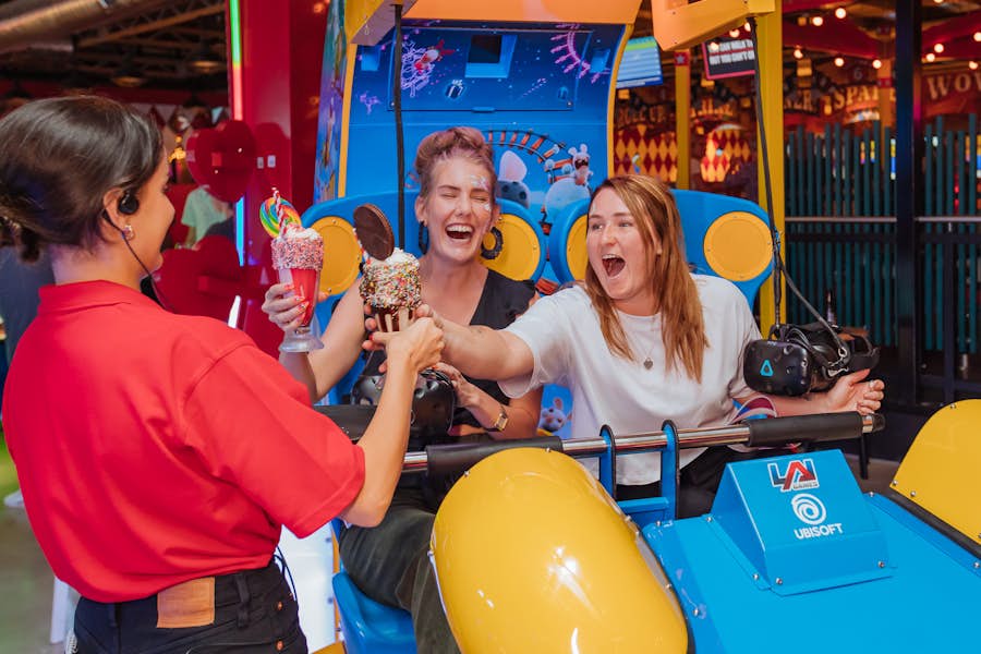 two girls on an arcade ride being served cocktails