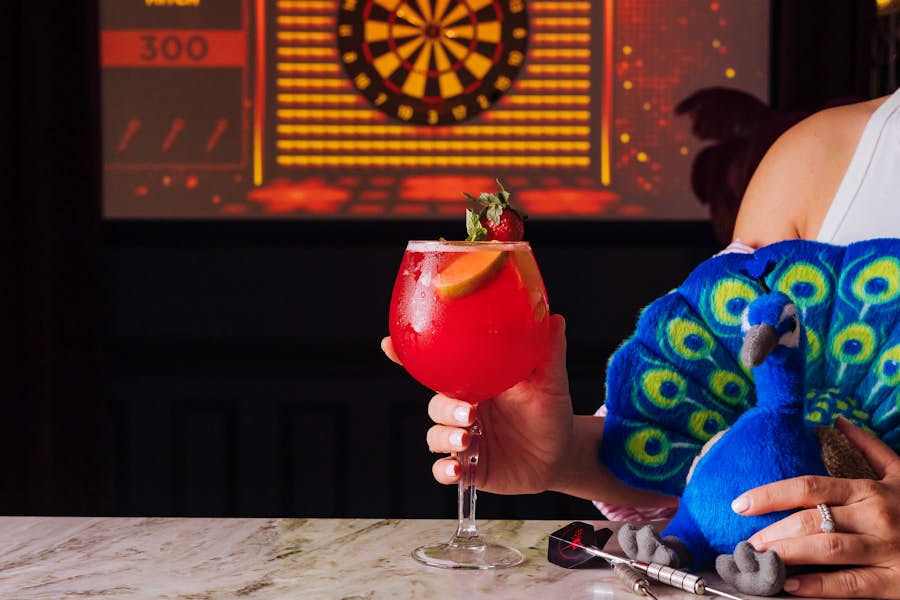 woman holding cocktail and peacock plush toy at la di darts