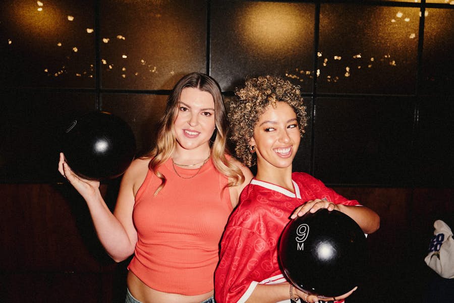 two girls holding bowling balls in the air and smiling at the camera