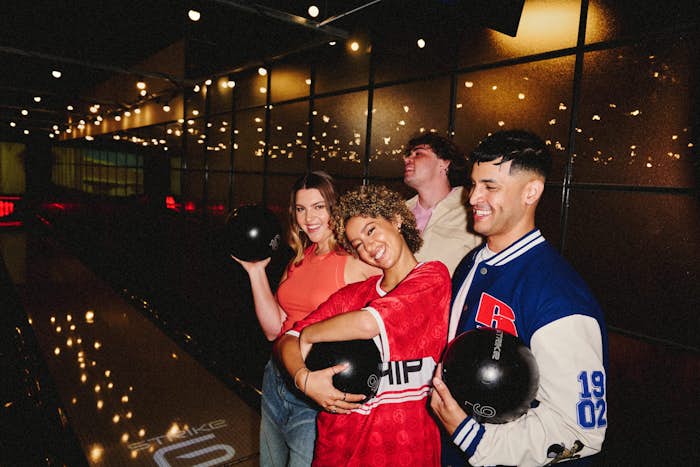 friends standing at a strike bowling lane, holding bowling balls and smiling