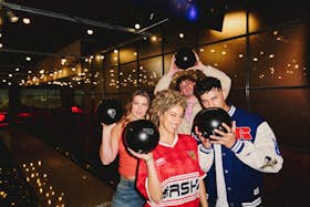 A group of 4 friends holding bowling balls and posing for the camera