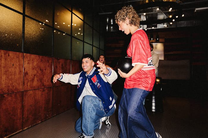man crouching after throwing a bowling ball and celebrating with a girl