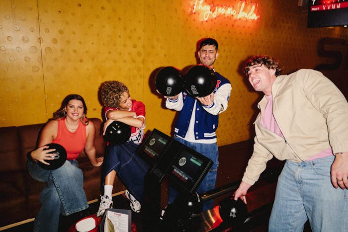 four friends relaxing by a lane couch with bowling balls at a strike party