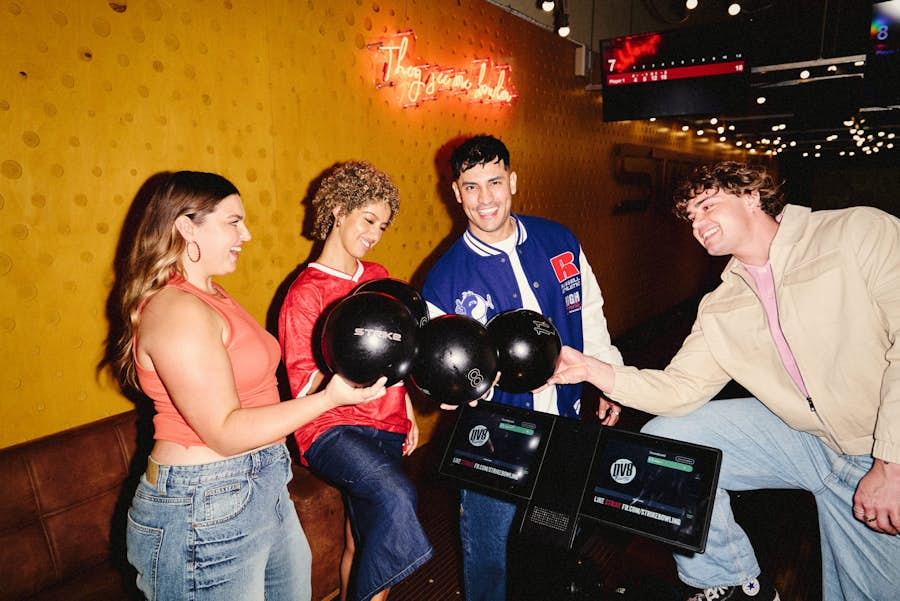 group of friends in a circle each holding a bowling ball and smiling