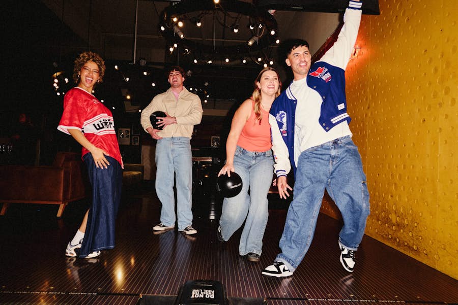 group of four friends on a bowling lane laughing and watching each other play
