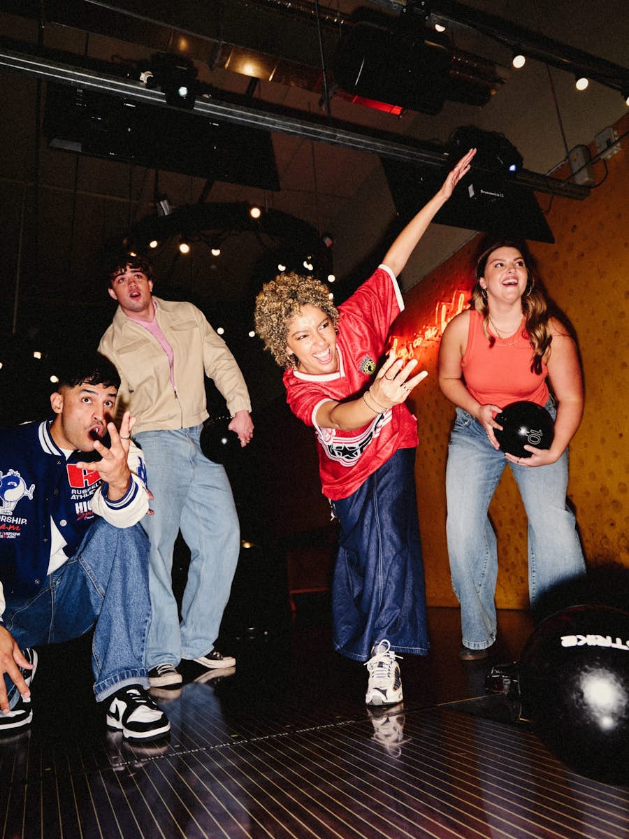 New Strike Shoot, a group of four friends holding bowling balls looking down an alley