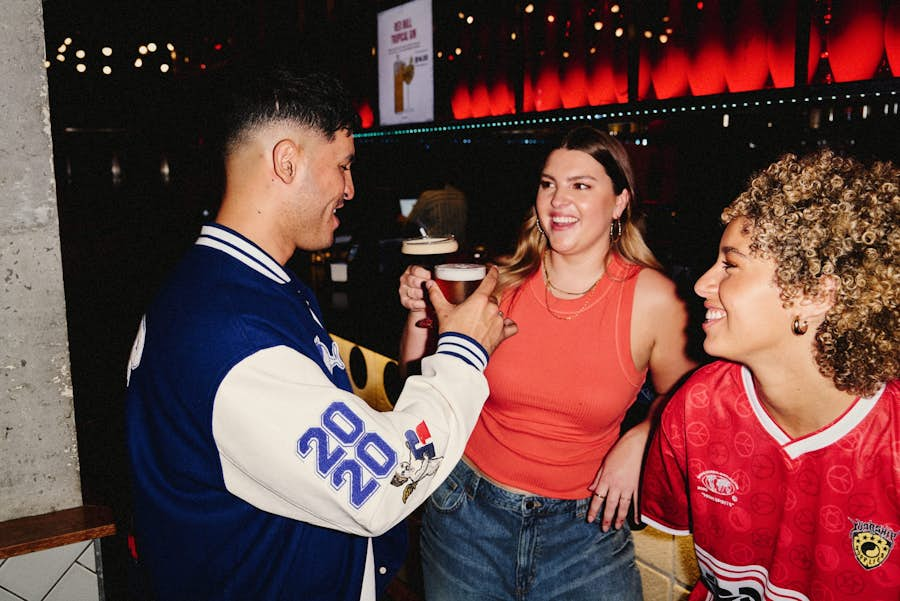 girl and guy toasting with a Pint and a cocktail while standing at the Strike Bar