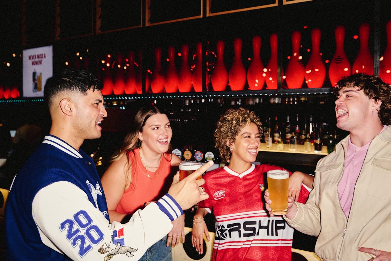 a group of friends standing and relaxing at the strike bar with beers before a game of bowling