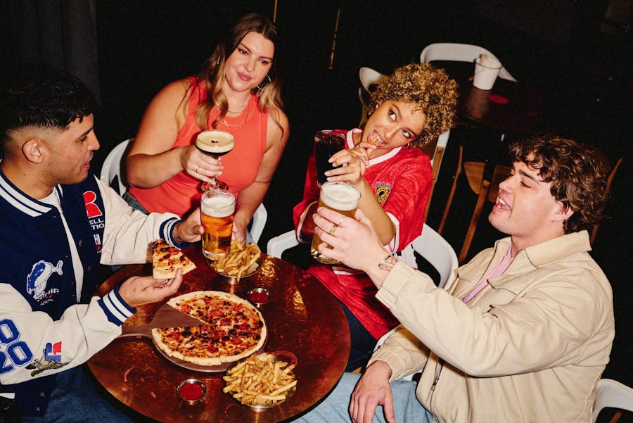 two guys and two girls toasting with drinks while enjoying pizza and fries