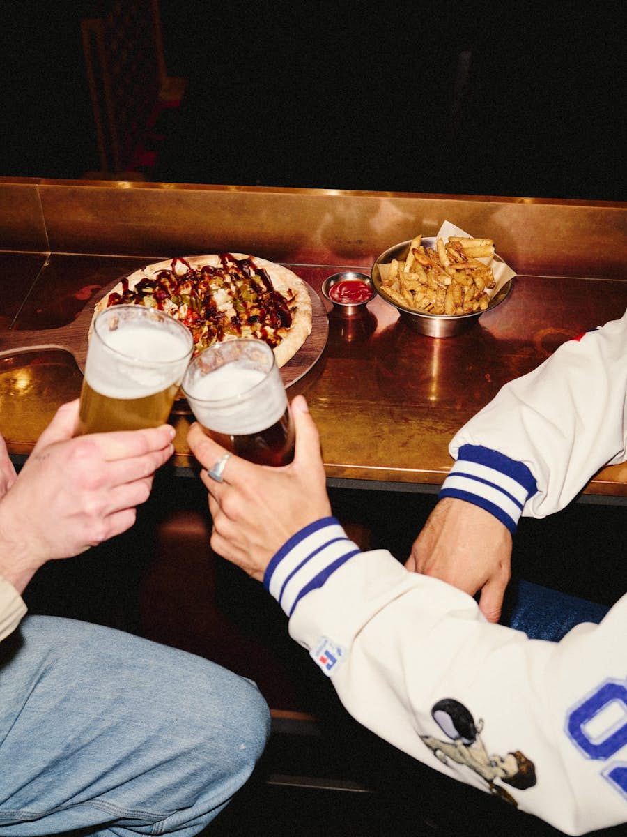 Two guys clinking their pints of beer while enjoying pizza, chips and dips
