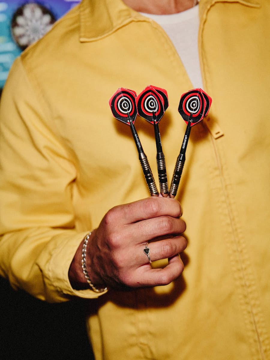 close up of man in yellow shirt holding three red and black darts by their tip