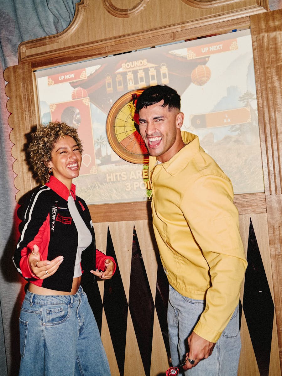 man and woman standing infront of interactive dart board and smiling at the camera