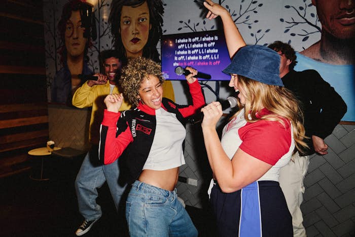 two girls and two men with microphones dancing, singing and jumping in a karaoke room