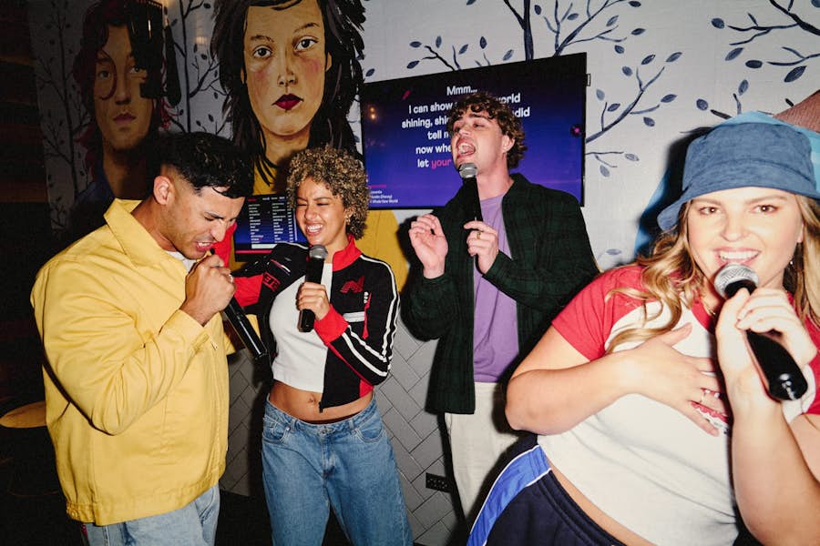 A group of four work colleagues in a strike karaoke room singing and dancing