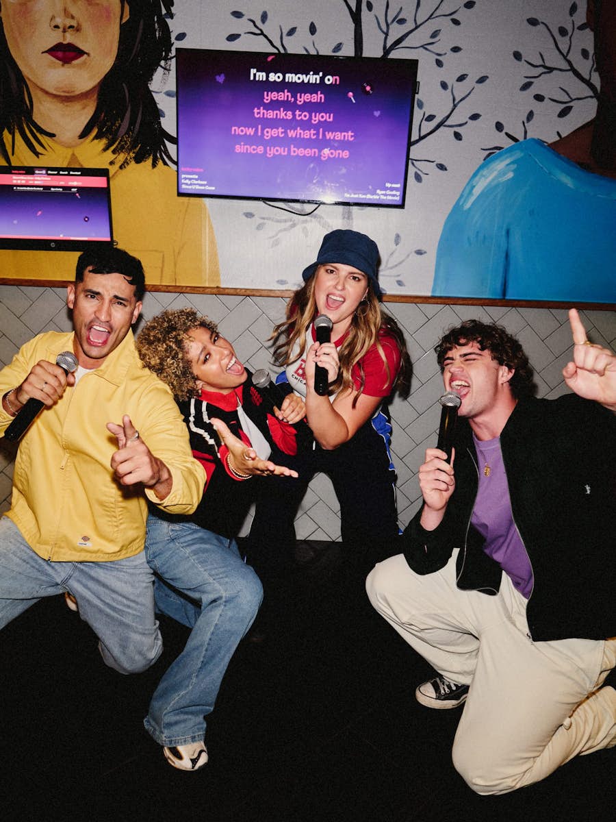 group of friends with microphones kneeling and singing towards the camera in a Karaoke room