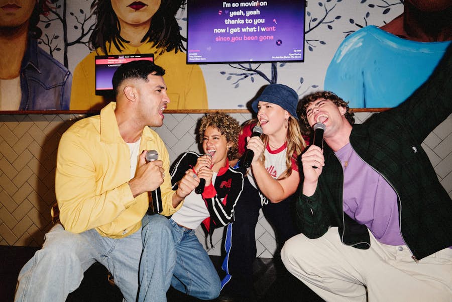four friends crouching and singing karaoke together