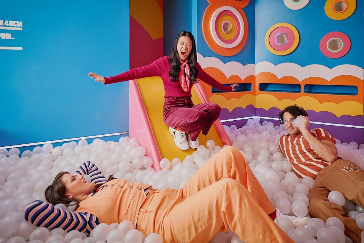 Hijinx Hotel Adore A Ball Pool room filled with white balls and multicoloured walls. There is a girl using the slide to get into the ball pit with her friends