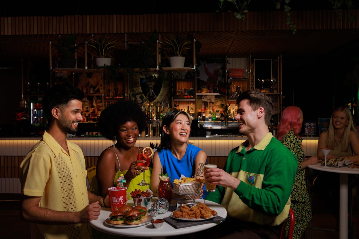Four people standing around a table eating and drinking at Holey Moley