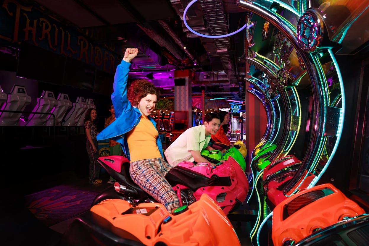 Man and woman playing on motorbike arcade game