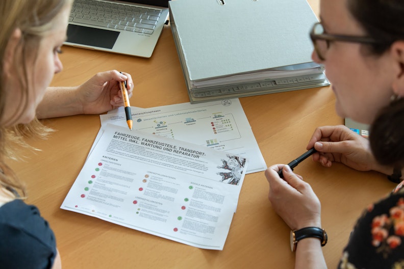 Zwei Frauen besprechen ein Merkblatt über die nachhaltige Beschaffung von Fahrzeugen
