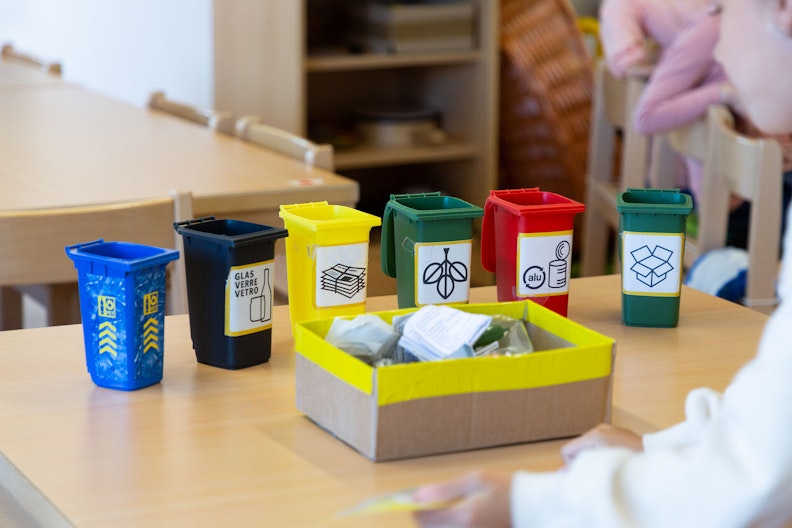 Mädchen greift mit beiden Händen in eine farbige Kartonbox und blickt nachdenkend nach oben.